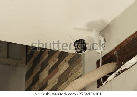 A close-up of a white Wi-Fi security camera with dual antennas installed on a building wall. This surveillance equipment provides 24 hours digital monitoring and safety for residential or commercial properties.