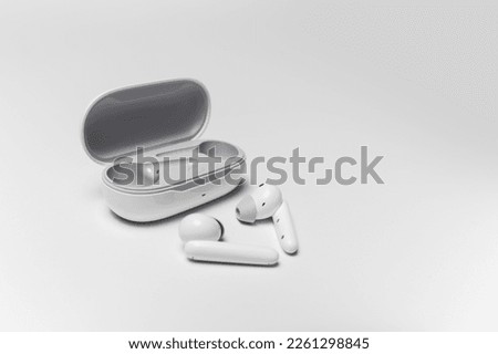 Close-up of white wireless earphones lying near opened charging case on grey background.