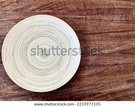 Close-up of a white wooden plate on the surface of a dark wooden tabletop. A wooden plate with a texture of concentric circles on a dark brown wooden table.
