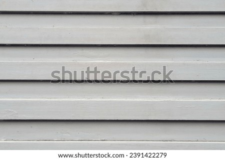 Close-up of a white wooden wall. The planks are vertical and have a beveled edge, which is a common type of siding called clapboard. Painted white, and the grain is still visible through the paint