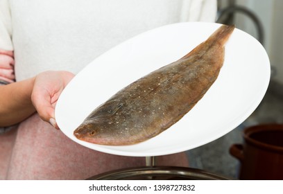 Closeup Of Whole Fresh Black Sole Fish On Plate In Hands Of Woman

