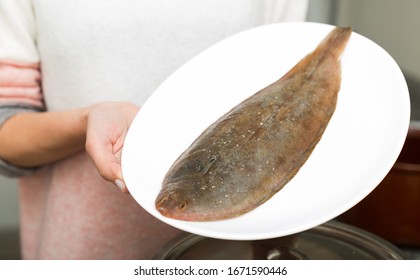 Closeup Of Whole Fresh Black Sole Fish On Plate In Hands Of Woman

