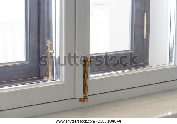 Close-up of a window frame. White modern\
plastic windows with golden latches. Home interior. Energy\
efficient, security profile, fresh air for\
home