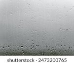 A close-up of a window pane speckled with water droplets, hinting at recent rainfall or misty conditions.