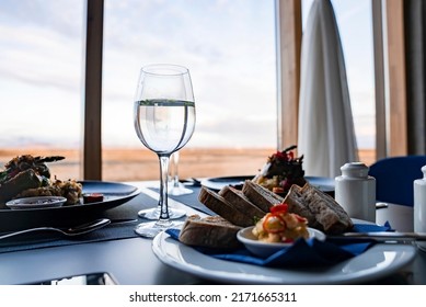 Close-up Of Wineglasses And Tasty Food On Dining Table. Gourmet Meal Is Served Against Window With View Of Sky. Concept Of Beautiful Catering In Restaurant At Luxurious Hotel.