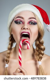Closeup winter portrait of girl in santa hat. Bright creative makeup. Positive emotions. Girl holding candy cane.