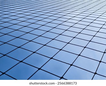 Close-up of a wire fence with a geometric pattern set against a clear blue sky, showcasing minimalist design. - Powered by Shutterstock