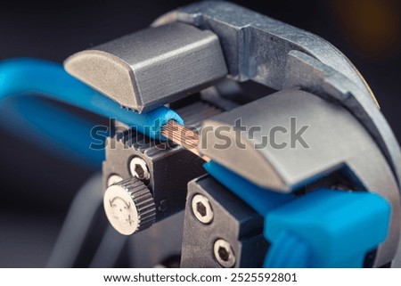Close-up of a wire stripper tool cutting a blue wire with exposed copper. Macro shot of electrical equipment.
