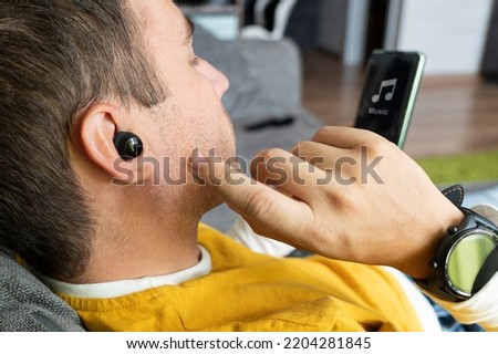 Close-up of wireless earphone in human ear on dark background. insert the earphone into the ear. listening to music with headphones.