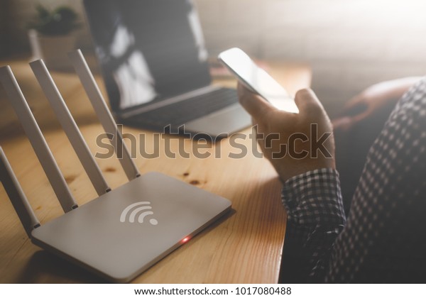closeup of a wireless router and a man using\
smartphone on living room at home\
ofiice