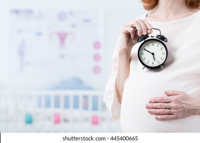 Close-up Of Woman After Forties In Pregnant Holding The Ticking Clock