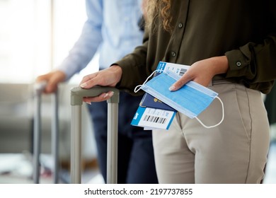 Closeup Of A Woman At The Airport To Travel During The Covid Pandemic With Luggage In Hand. Business Female Traveling For Work Standing With Passport, Plane Ticket And Face Mask To Board The Airplane