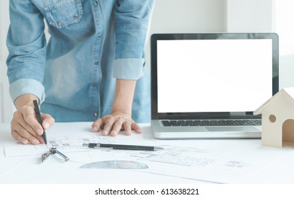 Close-up Woman Architect Drawing Blueprint On Work Space Wooden Table In Office With Empty Blank Screen Laptop