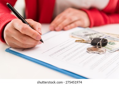 Closeup Of Woman Auto Dealer Signing Rental Contract In The Office. Car Key And Money On Papers. Shallow Depth Of Field.