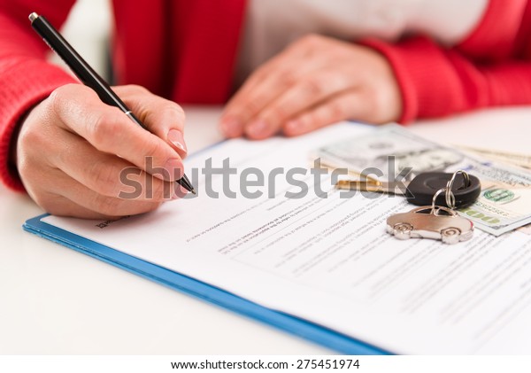 Closeup of\
woman auto dealer signing rental contract in the office. Car key\
and money on papers. Shallow depth of\
field.