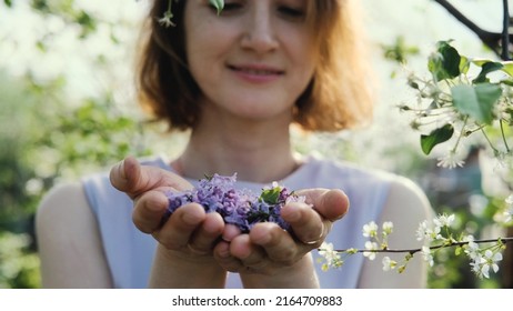 Close-up. A woman blows the petals of lilac flowers from her palms against the background of a spring park