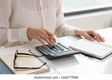Closeup of woman calculating expenses. Notebooks, glasses and calculator lying on desk. Finance concept. Cropped view.