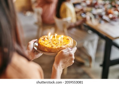 Close-up Of Woman Carrying Plate With Homemade Cake And Candles To The Table At The Birthday Party