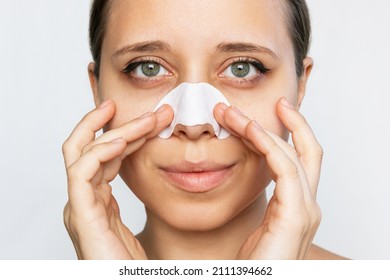 Close-up of a woman cleaning the skin of a face with nose strips from blackheads or black dots isolated on a white background. Acne problem, comedones. Enlarged pores on the face. Cosmetology concept