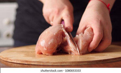 Close-up woman cuts chicken with a ceramic knife on a wooden Board. Female hands chef cutting raw chicken meat breast. - Powered by Shutterstock