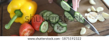 Close-up of woman cutting juicy cucumber on thin slices on wooden board. Fresh summer vegetables on kitchen. Tasty breakfast for family. Healthy nutrition and diet concept