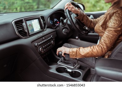 Close-up, woman driving a car includes a gearbox, reversing, starting to move in woods, leather jacket, automatic transmission. Touch screen navigation map app on monitor - Powered by Shutterstock