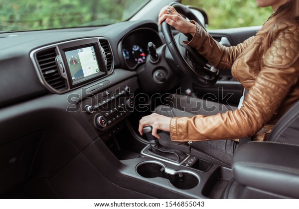 Close-up, woman driving a\
car includes a gearbox, reversing, starting to move in woods,\
leather jacket, automatic transmission. Touch screen navigation map\
app on monitor