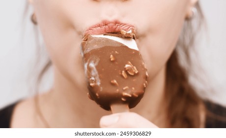 Close-up of Woman Eating Chocolate Ice Cream. Close-up of a woman's lips biting into a chocolate-covered ice cream with nuts on a stick - Powered by Shutterstock