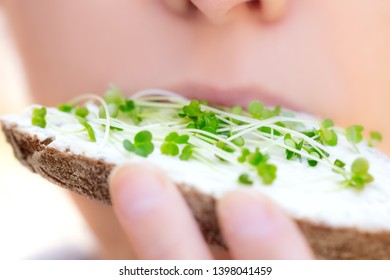 Closeup Of An Woman, Eating A Sandwich Or Bread With Fresh, Healthy Microgreens Like Garlic Seedling