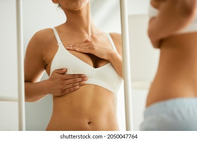 Close-up of woman examining her breasts while looking herself in am mirror.