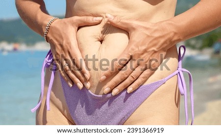 Closeup of woman with fat on belly wearing biking touching her body on the sea beach.