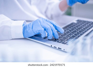 Closeup woman female scientist's hand blue protective glove using laptop for recording scientific medical experiment research from laboratory - Powered by Shutterstock