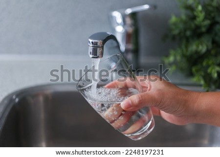 Closeup Woman filling glass with fresh water from faucet in kitchen. Drinking tab water concept.