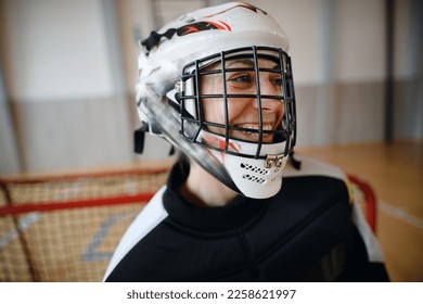Close-up of woman floorball goalkeeper in helmet concetrating on game in gym.