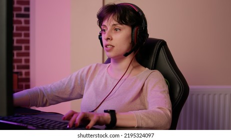 Closeup Of Woman With Gaming Headset Playing Multiplayer First Person Shooter Streaming Gameplay On Professional Pc Setup. Gamer Girl Looking At Computer Screen While Talking To Team In Tournament.