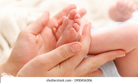 Closeup of woman gently stroking with hand tiny feet of her newborn baby son with perfect skin. Concept of family happiness and loving parents with little children. - Shutterstock ID 1900456306