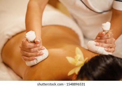 Close-up of woman getting back massage with detox herbal compresses at spa salon.