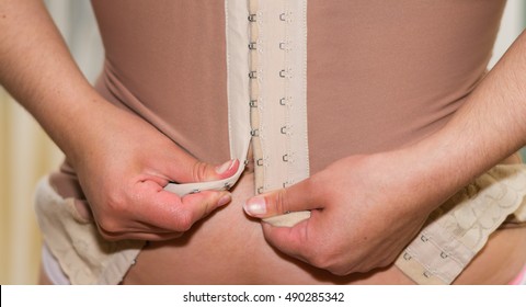 Closeup woman getting dressed, hooking on corset hooks using hands behind back, weightloss concept