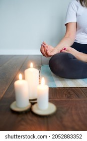 Close-up of a woman in gray pants sitting in a lotus position and meditating by candlelight.