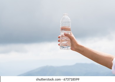 Closeup Woman Hand Holding Bottle Of Water On Sky Background.