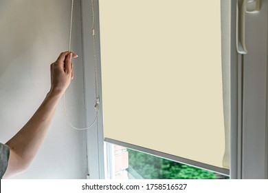 Closeup of woman hand opens roll blinds on window in the modern interior. Roll louvers on the window. - Shutterstock ID 1758516527