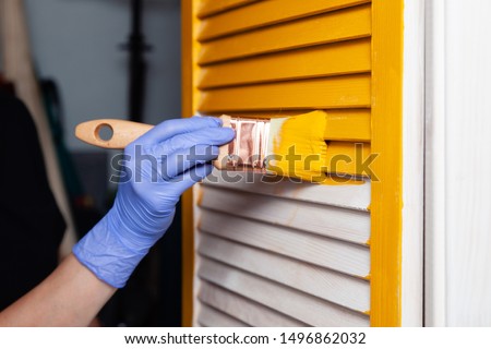 Closeup woman hand in purple rubber glove with paintbrush painting natural wooden door with yellow paint, creative design house renovation theme. How to Paint Wooden Surface. Selected focus