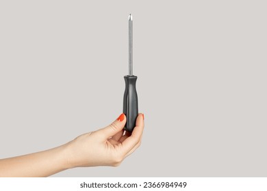 Closeup of woman hand showing black metal and plastic tool screwdriver for repair. Indoor studio shot isolated on gray background. - Powered by Shutterstock