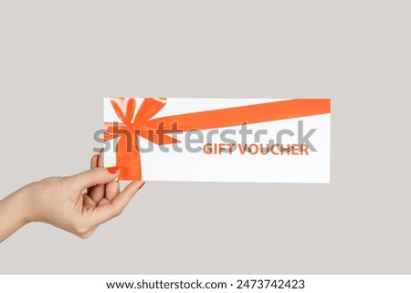 Closeup of woman hand showing paper card, gift voucher, present for free shopping. Indoor studio shot isolated on gray background.