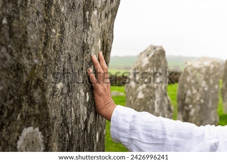 Closeup of woman hand touching large stone belonging to the Drombeg megalithic circle on her road visit to County Cork