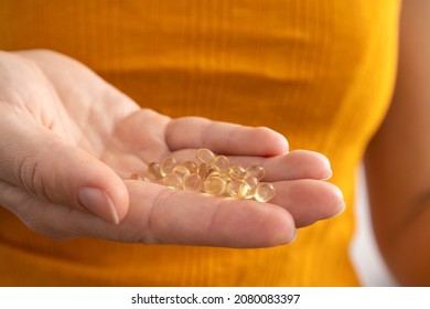 Closeup Of Woman Hand And Vitamin D Capsules Against Bright Yellow Shirt.Concept Of Deficiency Of Vitamins