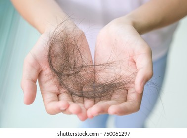 Close-up of woman hand in white t-shirt hold loss hair, after taking shower, concepts of loosing hair or breast cancer.  Close-up of cancer patient girl hands showing her lost hair.