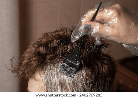 Closeup woman hands dyeing hair using a black brush. Colouring of white hair at home