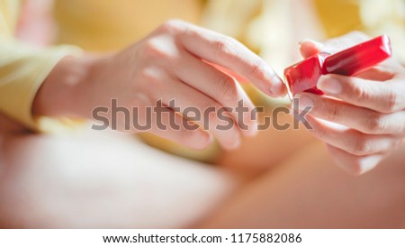 Close-up of woman hands hold red nail paint bottle.