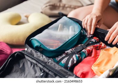 Closeup Woman Hands Holding Mesh Cosmetic Bag And Try To Put Them In Luggage. Packing To Go On A Getaway Vacation.